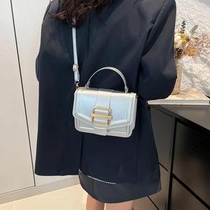Minimalist metallic silver crossbody square bag with gold buckle on a model in indoor setting