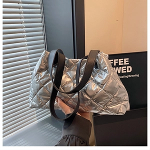 Detail of silver quilted puffer bag with glossy finish and black leather shoulder strap