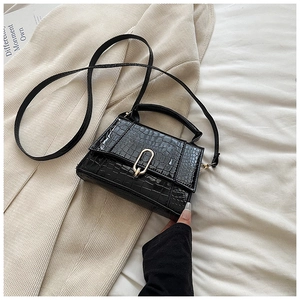 Détail du petit sac noir croco avec fermoir doré sur un manteau de couleur beige
