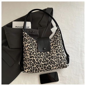 Leopard print tote bag with black leather flap and snap closure on a grey blazer