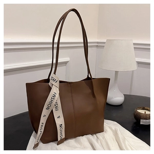 Close-up of a large brown faux leather tote bag with stylish logo ribbon and slim straps