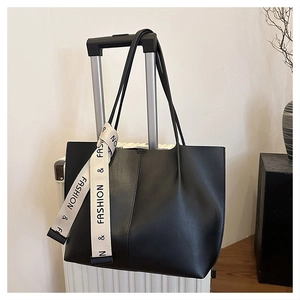 Large black faux leather tote bag with a beige ribbon tied to the handle on a suitcase