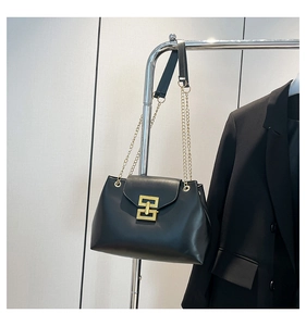 Detail of black leather tote bag with a golden geometric metal buckle and chain strap