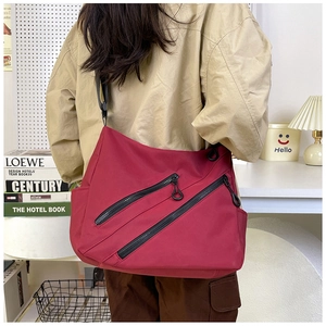 Close-up of a large dark red nylon crossbody bag with dual diagonal zipper pockets
