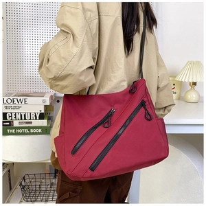 Detail of dark red tote bag with dual parallel zippers and wide strap on model