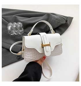 Close-up of white croc-embossed patchwork handbag with elegant gold metal clasp