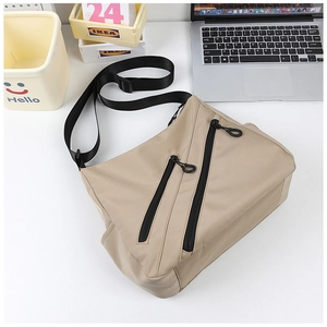 Close-up of khaki nylon tote bag with black zippers and adjustable straps on a desk