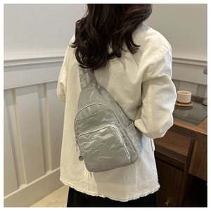 Detail view of the silver pleated backpack featuring a modern crinkle fabric texture on a model