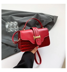 Detail of red croc-effect leather handbag with gold T-shaped clasp and handle