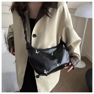 Gros plan du sac hobo en cuir mat noir avec détails papillons argentés sur modèle