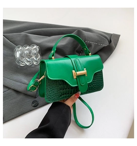 Detail of green faux-crocodile texture and gold H-buckle on a stylish crossbody handbag