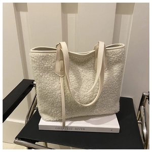 Detail of soft cream faux shearling tote bag resting on black chair with book