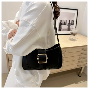 Detail view of black underarm bag with gold metal buckle on a white sweatshirt