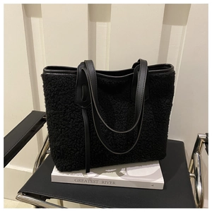 Detail of black faux shearling tote bag with synthetic leather straps on a chair
