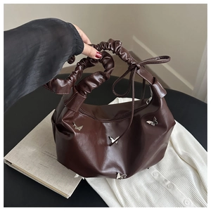 Détails d'un sac cabas froncé marron foncé avec des breloques papillon argentées et nœuds