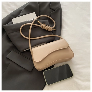 Detail of beige faux leather shoulder bag with curved flap and knot strap detail
