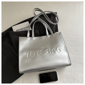 Detail of silver metallic tote bag with embossed TOTE BAG lettering and glossy finish