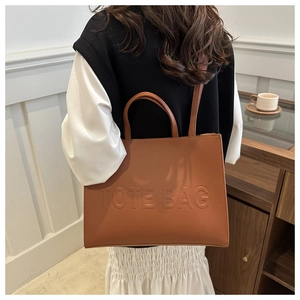 Detailed close-up of brown textured tote bag with embossed lettering and shoulder strap