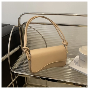 Detail of minimalist beige handbag with knotted handle and curved flap on shelf