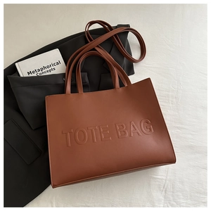 Detailed view of brown textured leather tote bag with embossed TOTE BAG text and long strap