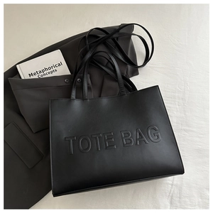 Detail of black faux leather tote bag featuring debossed text on a white fabric surface