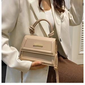 Detail of beige faux leather handbag featuring a gold metal trim and unique knot handle design