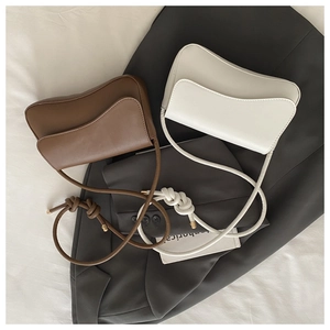 Detail of minimalist wave-cut leather bags in brown and beige with knot strap accents