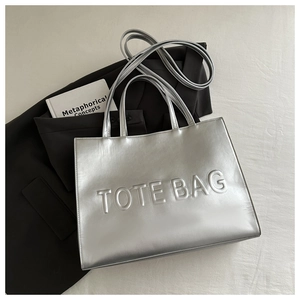 Close-up of silver metallic tote bag with embossed letters on black blazer background