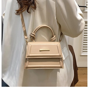 Detail of beige leather crossbody bag with knot handle and gold hardware on white blazer