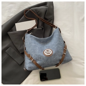 Detail of blue denim canvas tote bag with brown leather strap and metal M logo