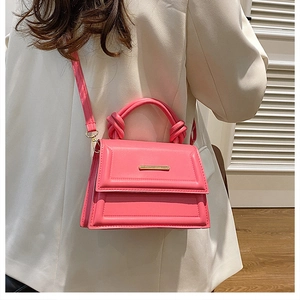 Pink crossbody bag with a knotted handle shown on a white blazer for a chic look