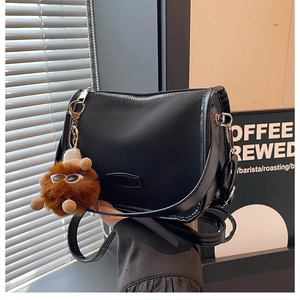 Detail of black crescent crossbody bag with silver zipper and brown plush charm