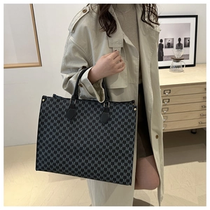 Détail du cabas gris à imprimé monogramme avec anses en cuir noir porté par un mannequin