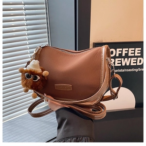 Detail of a brown crescent shoulder bag with a fashion tag and plush bear charm