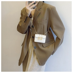 Close-up of white leather mini bag with gold chain strap worn over a brown blazer