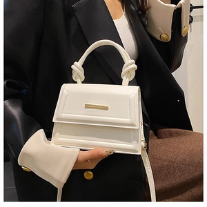 Detail of white leather crossbody bag with knot handle and gold metal bar accent