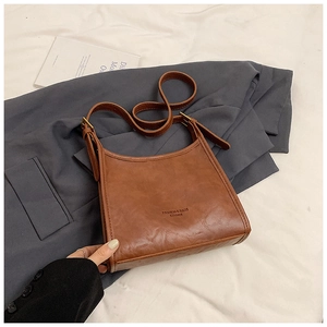 Detail view of brown vintage leather tote bag with metal buckle on a grey blazer