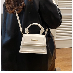 Close-up of cream square handbag with horizontal embossed lines and knotted handle