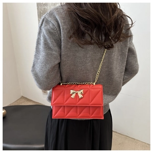 Détail d'un sac bandoulière rouge matelassé avec boucle papillon dorée porté par un mannequin