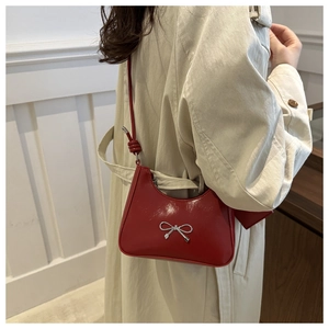 Detail of glossy red underarm bag with silver bow accent and knotted shoulder strap