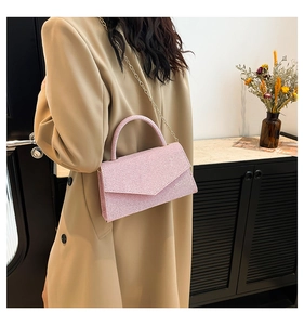 Detail of pink glitter handbag featuring triangle flap and gold chain strap on model