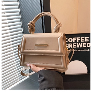 Detailed view of beige faux leather handbag featuring a gold bar and knotted top handle