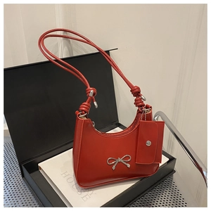 Close-up of a red glossy leather underarm bag with silver bow and matching mini pouch