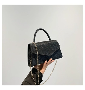 Detail of black sequin envelope bag with golden chain strap and sparkling texture