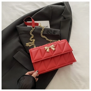 Détail du sac rouge matelassé avec fermoir papillon doré et bandoulière en chaîne