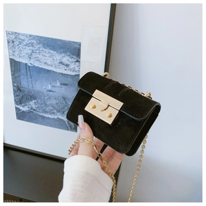 Detail of a mini black suede crossbody bag with gold chain and metal snap closure