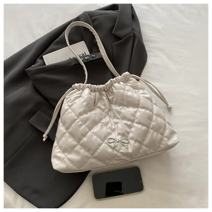 Close-up of quilted cream shoulder bag with drawstring and silver bow detail