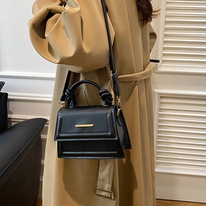 Minimalist black crossbody bag with knot handle and gold hardware on a model