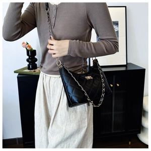 Black quilted crossbody bag with gold chain strap shown on model in a modern interior