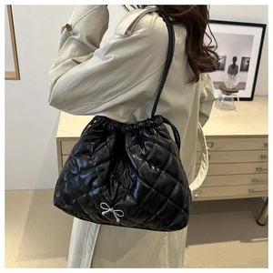 Detail of black quilted shoulder bag with drawstring closure and silver bow ornament